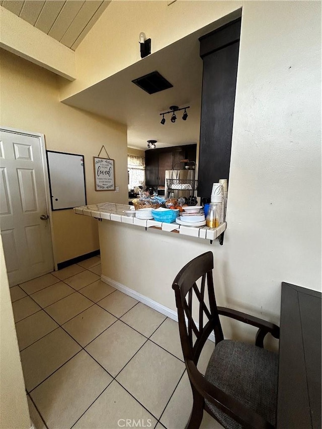 kitchen with light tile patterned floors, a peninsula, lofted ceiling, tile counters, and track lighting