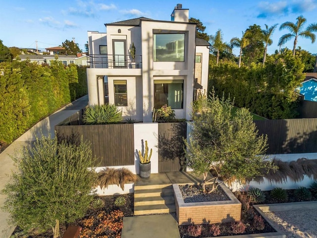 contemporary home featuring fence private yard, a chimney, a balcony, and stucco siding