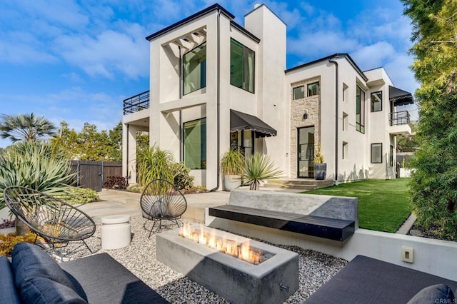 back of property featuring a fire pit, fence, stucco siding, a yard, and stone siding