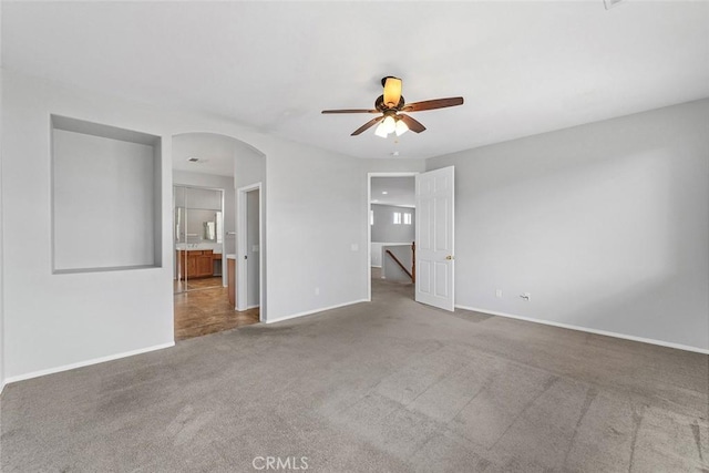 unfurnished bedroom featuring baseboards, arched walkways, and carpet