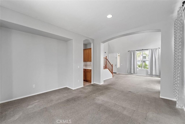 spare room with arched walkways, stairway, baseboards, and carpet floors