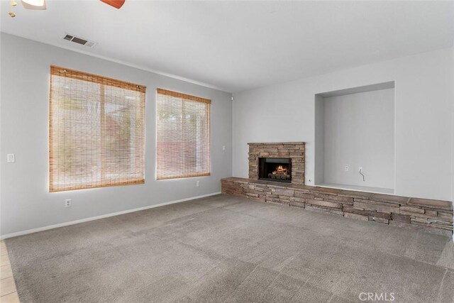 unfurnished living room featuring carpet, baseboards, a stone fireplace, and visible vents
