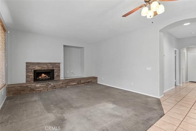 unfurnished living room with baseboards, arched walkways, a ceiling fan, a fireplace, and tile patterned floors