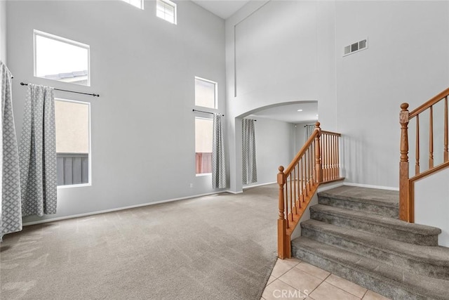 stairs with a towering ceiling, baseboards, carpet floors, visible vents, and arched walkways