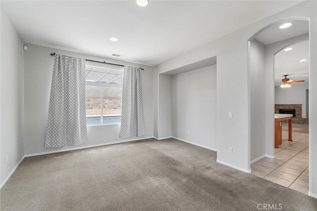 empty room featuring arched walkways, carpet floors, baseboards, and ceiling fan