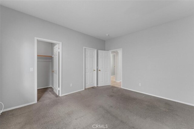 unfurnished bedroom featuring a spacious closet, carpet, and baseboards