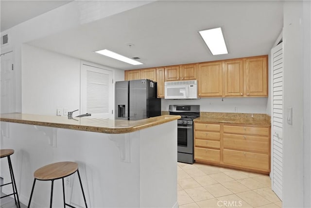 kitchen featuring a kitchen breakfast bar, kitchen peninsula, light tile patterned floors, appliances with stainless steel finishes, and light brown cabinetry