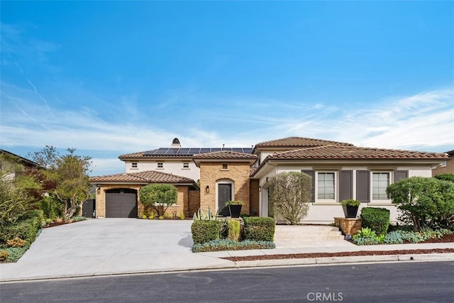 mediterranean / spanish-style house with roof mounted solar panels, a tile roof, driveway, and stucco siding