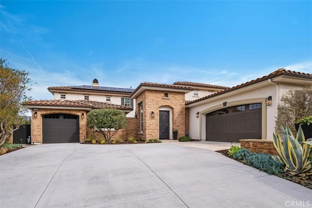 mediterranean / spanish-style home featuring concrete driveway, stone siding, a tile roof, roof mounted solar panels, and stucco siding