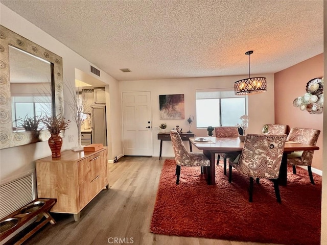 dining room featuring a textured ceiling, a notable chandelier, and light hardwood / wood-style floors