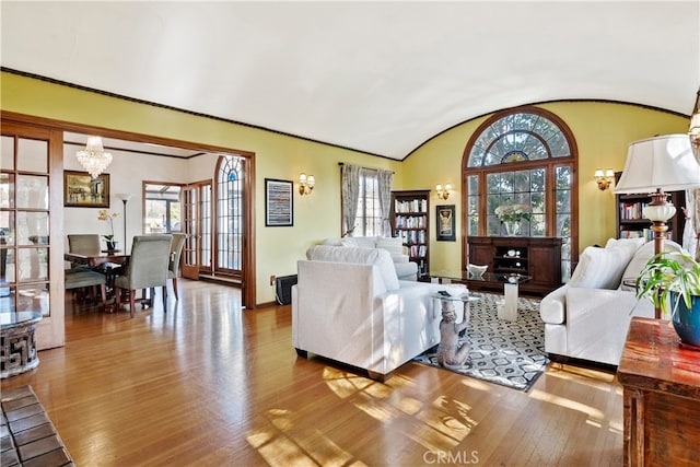 living area with vaulted ceiling, wood-type flooring, baseboards, and a notable chandelier