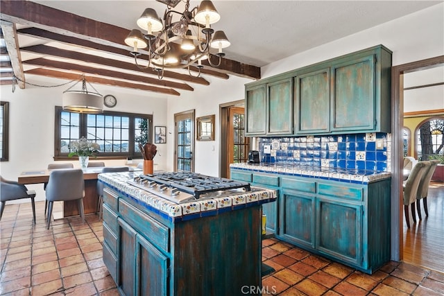 kitchen with stainless steel gas stovetop, a center island, beam ceiling, backsplash, and pendant lighting