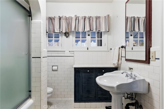 bathroom featuring bath / shower combo with glass door, tile walls, and toilet