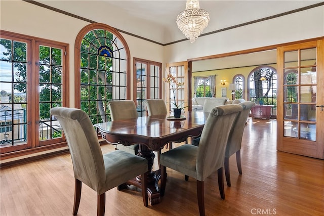 dining area featuring ornamental molding, light wood-type flooring, a chandelier, and french doors