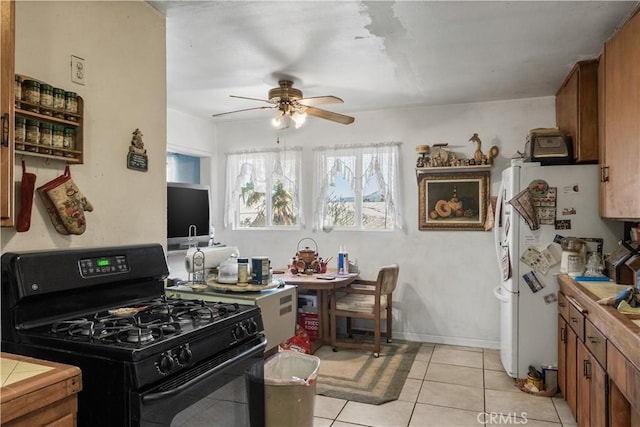 kitchen featuring tile countertops, white refrigerator, ceiling fan, black gas stove, and light tile patterned floors