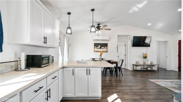 kitchen featuring lofted ceiling, a peninsula, white cabinets, an AC wall unit, and stainless steel microwave