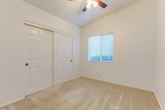 unfurnished bedroom with a closet, light colored carpet, a ceiling fan, vaulted ceiling, and baseboards