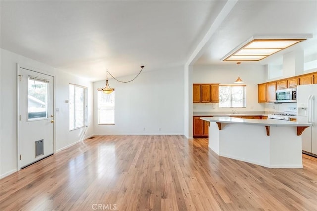 kitchen featuring white appliances, a kitchen breakfast bar, brown cabinets, a center island, and light countertops