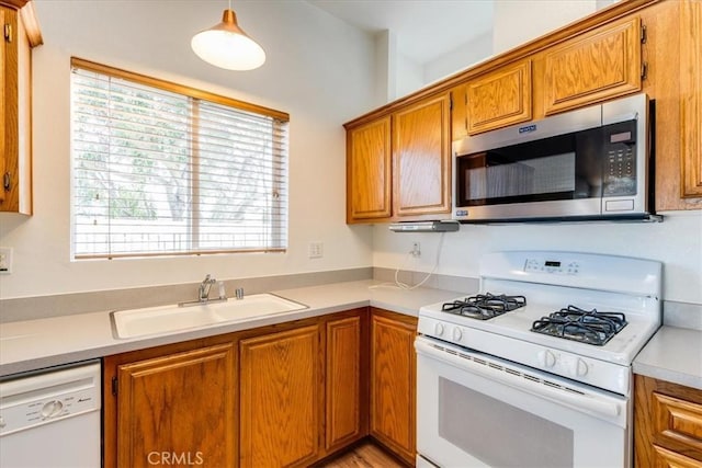 kitchen featuring light countertops, hanging light fixtures, brown cabinetry, a sink, and white appliances