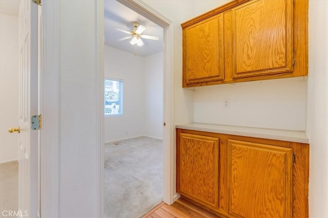 kitchen with ceiling fan, light countertops, light colored carpet, and brown cabinets