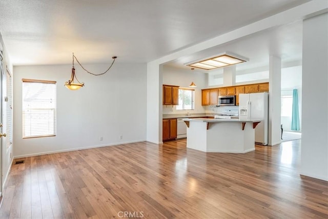 kitchen with hanging light fixtures, white appliances, brown cabinetry, and a kitchen bar