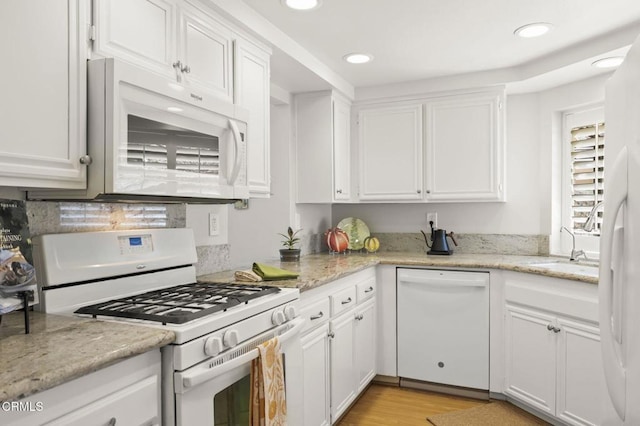 kitchen with white appliances, light wood-type flooring, white cabinetry, and light stone countertops