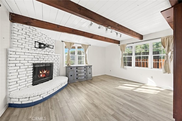 unfurnished living room with beamed ceiling, a brick fireplace, rail lighting, and light wood-style floors