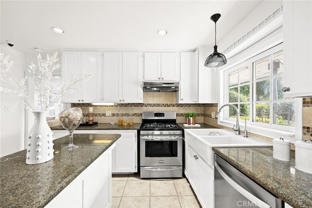 kitchen featuring decorative light fixtures, appliances with stainless steel finishes, white cabinetry, dark stone countertops, and under cabinet range hood