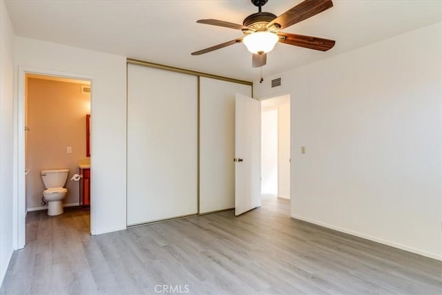 unfurnished bedroom with ensuite bathroom, light wood-type flooring, a closet, and ceiling fan