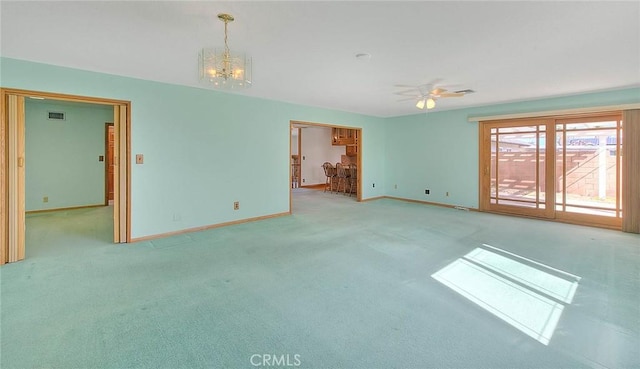 carpeted spare room featuring ceiling fan with notable chandelier