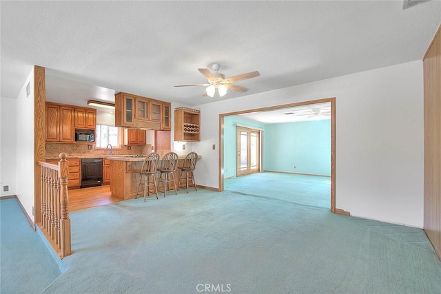 kitchen featuring kitchen peninsula, light colored carpet, black dishwasher, ceiling fan, and a kitchen breakfast bar