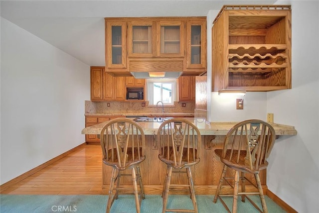 kitchen with backsplash, a kitchen breakfast bar, black microwave, light hardwood / wood-style floors, and kitchen peninsula