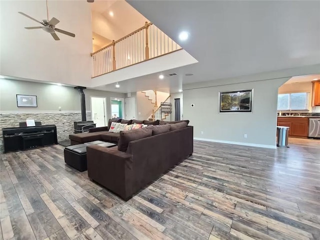 living room with stairs, wood finished floors, a wood stove, and a ceiling fan