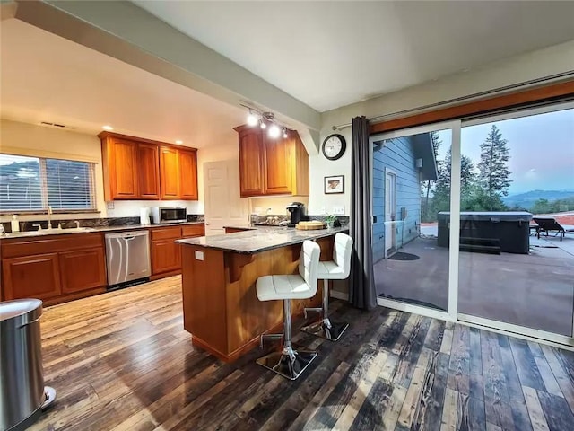 kitchen featuring stainless steel appliances, dark countertops, a sink, and a kitchen breakfast bar