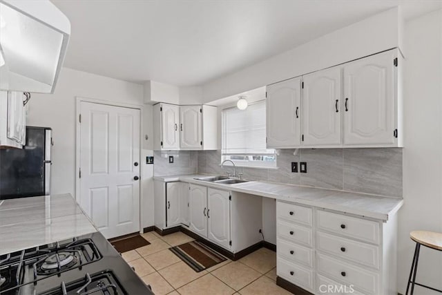 kitchen with tasteful backsplash, white cabinets, light tile patterned flooring, stainless steel refrigerator, and sink