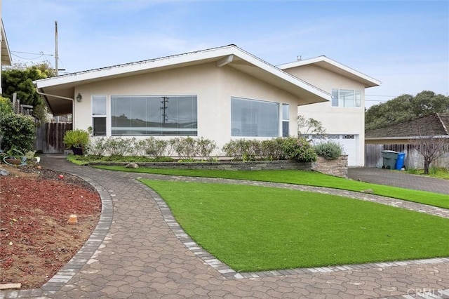 view of front of house featuring an attached garage, driveway, a front lawn, and stucco siding