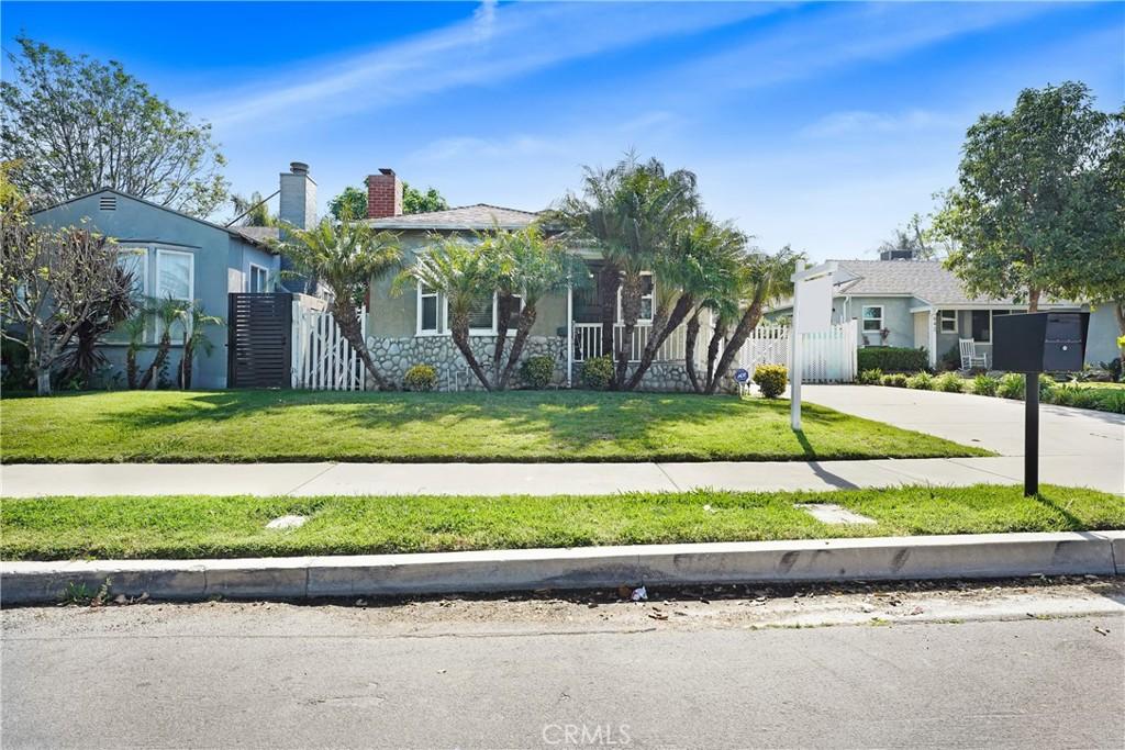 obstructed view of property with a front lawn, a chimney, concrete driveway, stucco siding, and fence