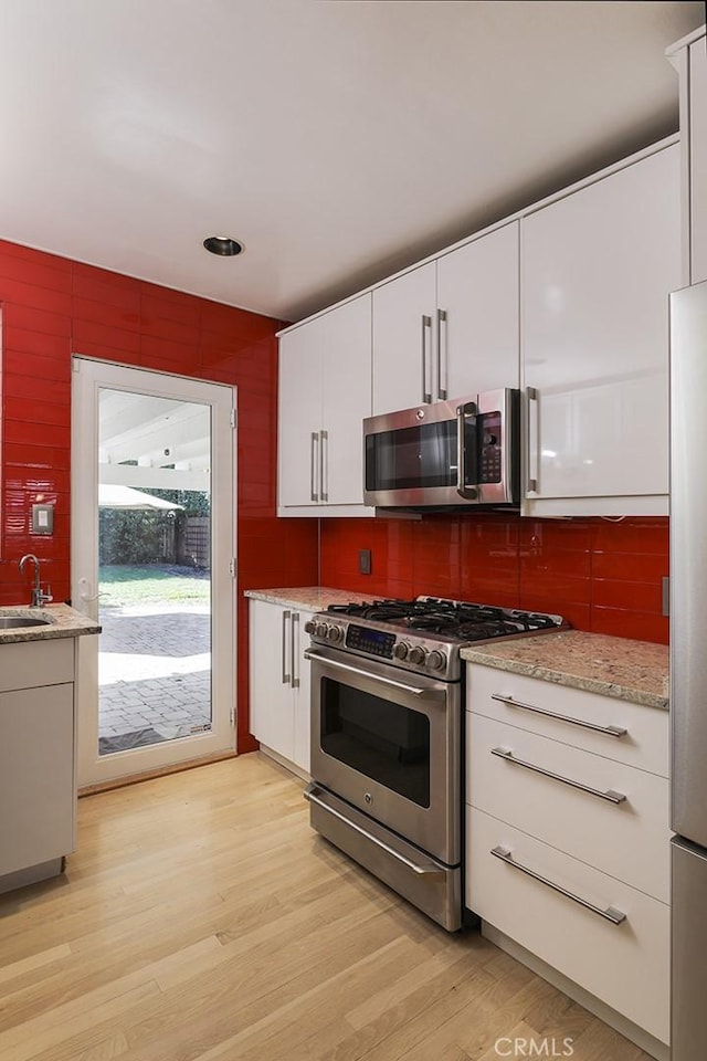 kitchen featuring sink, white cabinets, stainless steel appliances, and light wood-type flooring