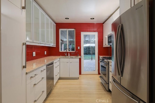 kitchen with white cabinetry, light wood-type flooring, stainless steel appliances, sink, and decorative backsplash