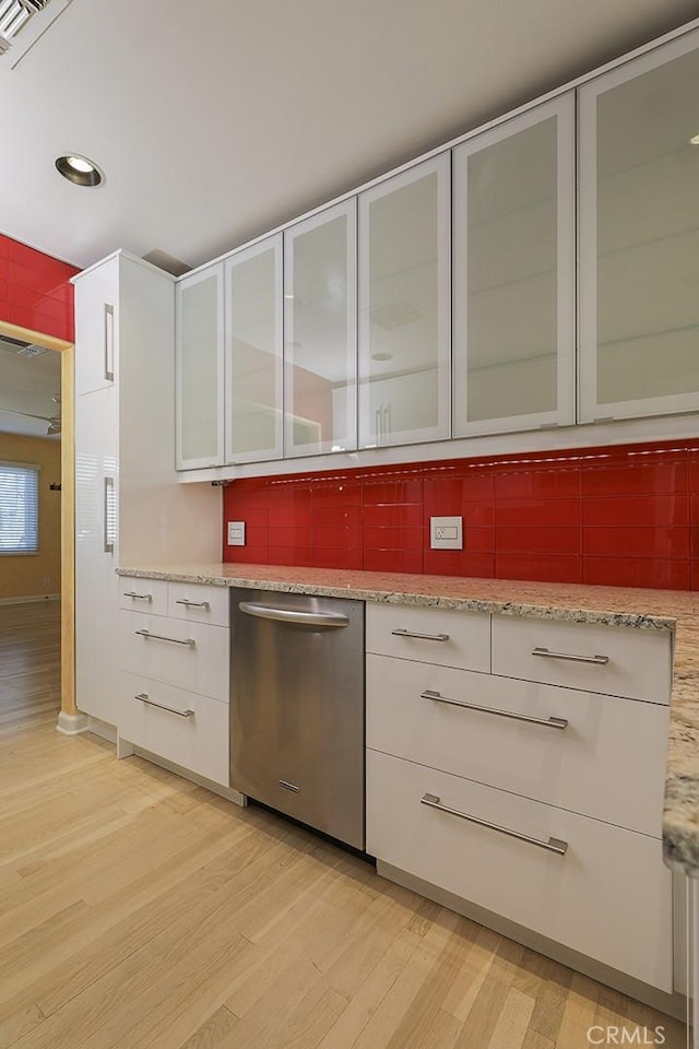 kitchen featuring light stone countertops, stainless steel dishwasher, backsplash, light wood-type flooring, and white cabinetry