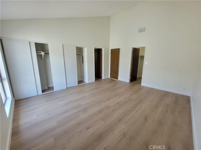 unfurnished bedroom with high vaulted ceiling, light hardwood / wood-style floors, and multiple closets