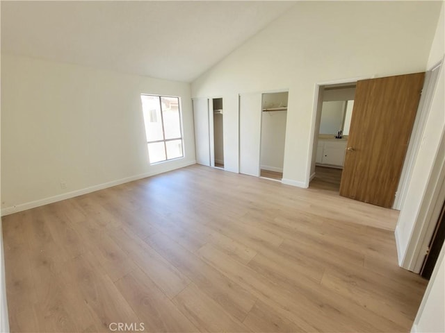 unfurnished bedroom featuring two closets, high vaulted ceiling, and light hardwood / wood-style flooring