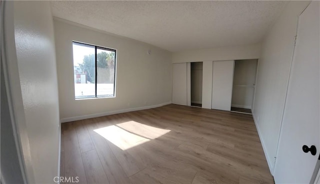 unfurnished bedroom featuring a textured ceiling, light hardwood / wood-style floors, and multiple closets