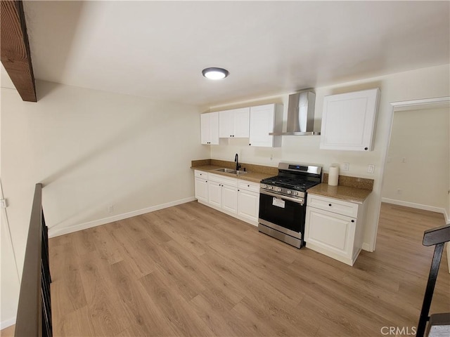 kitchen featuring sink, white cabinets, wall chimney exhaust hood, and stainless steel gas range