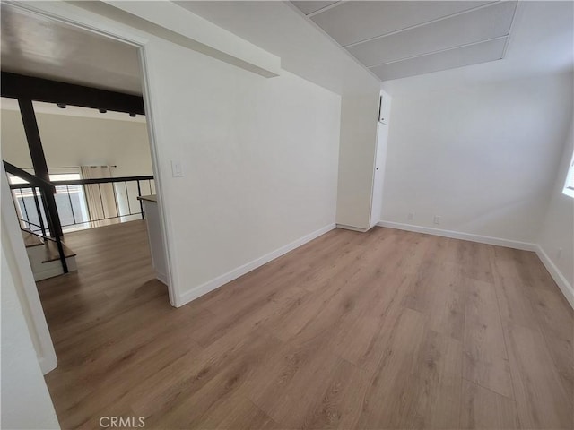 empty room featuring light wood-type flooring and beamed ceiling