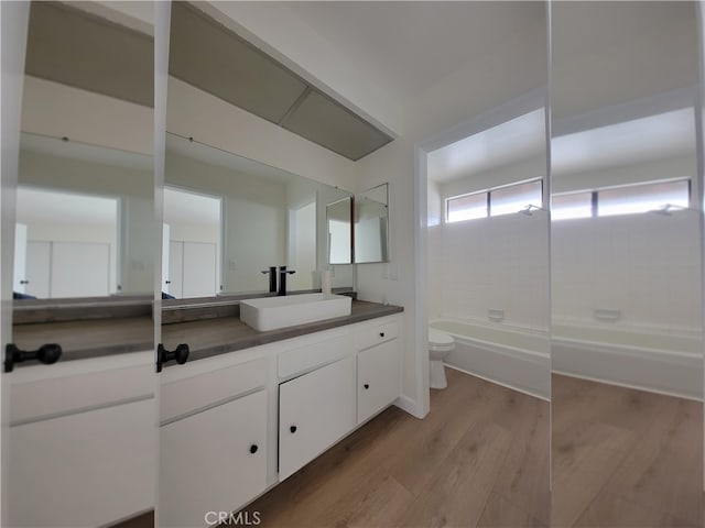 full bathroom featuring hardwood / wood-style flooring, tiled shower / bath combo, vanity, and toilet