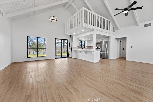 unfurnished living room with ceiling fan with notable chandelier, light wood-type flooring, vaulted ceiling with beams, and wood ceiling