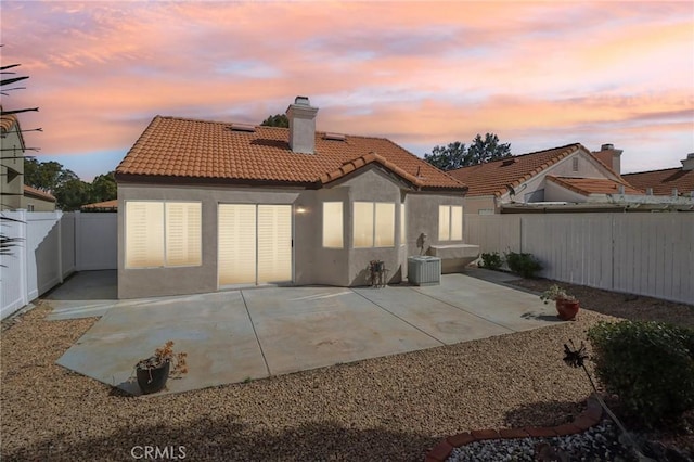 rear view of house with a patio, a chimney, stucco siding, a fenced backyard, and a tiled roof