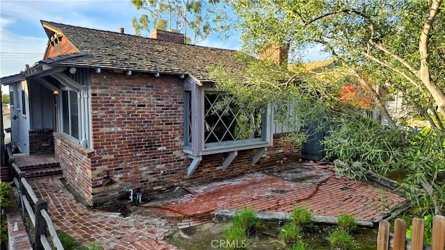 view of side of home featuring a patio area, a chimney, fence, and brick siding