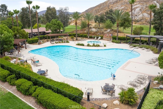 pool featuring a community hot tub, fence, a mountain view, and a pergola